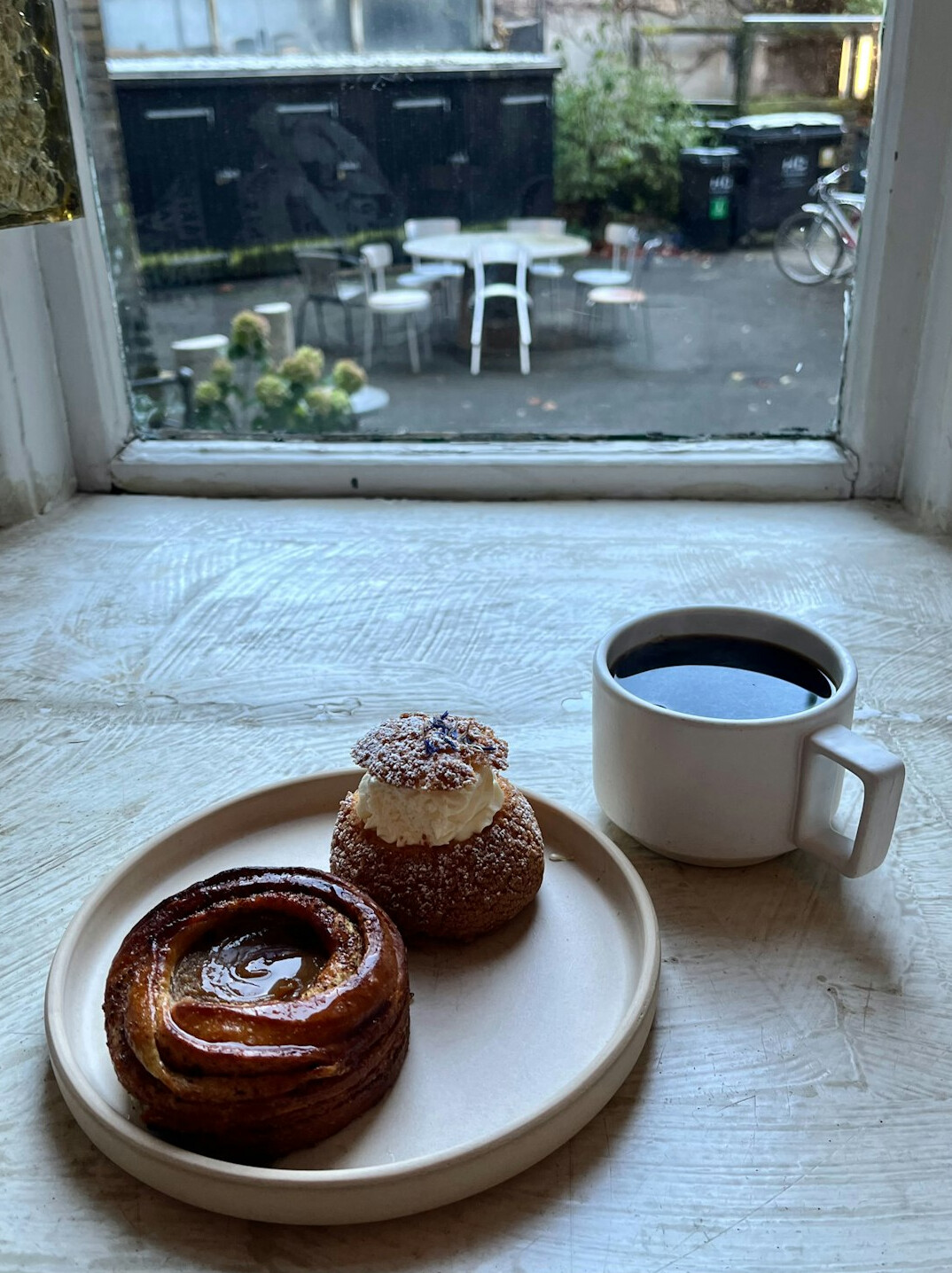 Cup of coffee and pastry on a wooden table by a window in a Danish cafe